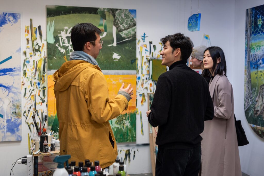 Three students discuss art while standing in front of abstract paintings hung on a wall. 